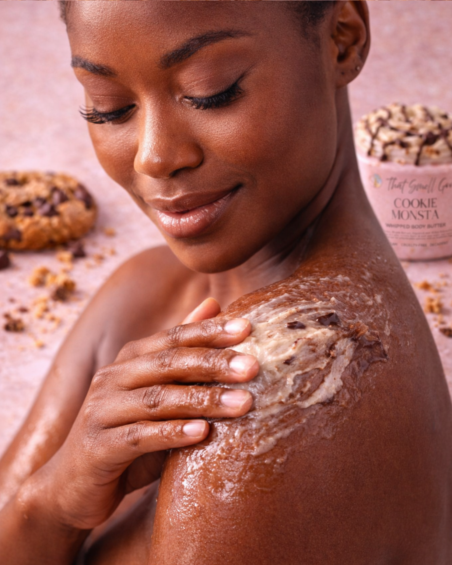 Woman applying Cookie Monsta Body Butter to her shoulder with cookies and a jar in the background.